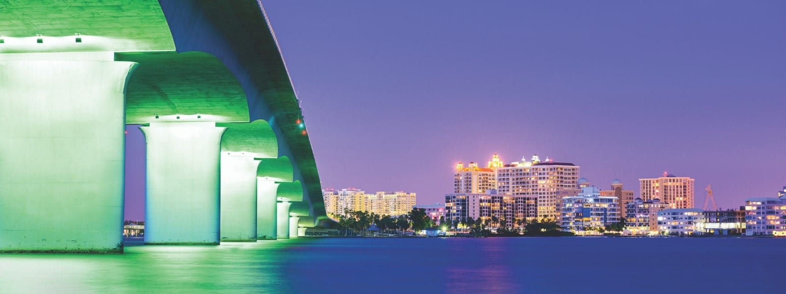 The Sarasota bay at sunset lit up with the bottom of the bridge on the left and the city lights straight ahead